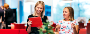 Two women sitting on a red couch and looking at ipad